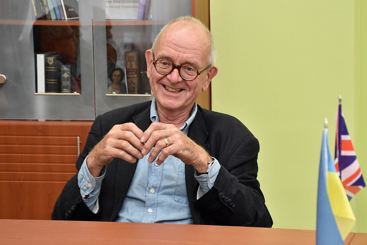 Henry Marsh smiling at a desk, with Ukrainian and British flags beside him.