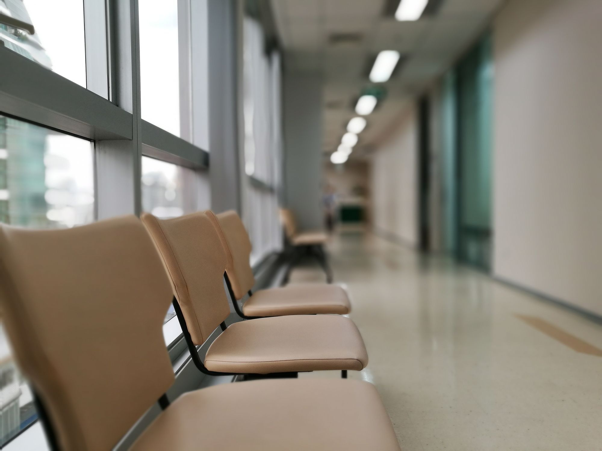 A row of empty waiting chairs along a bright hospital corridor.