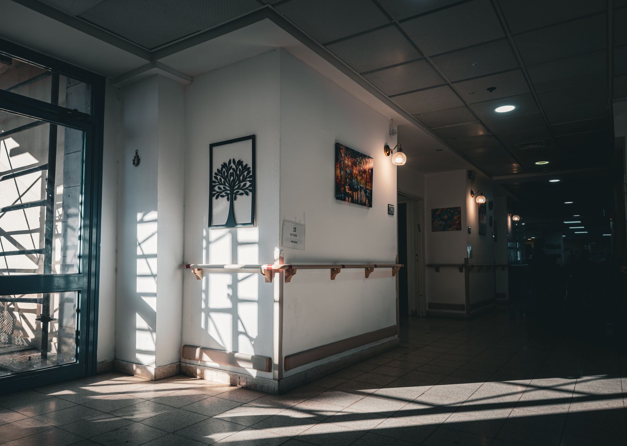 A quiet hospital corridor with sunlight falling across the floor from tall windows.